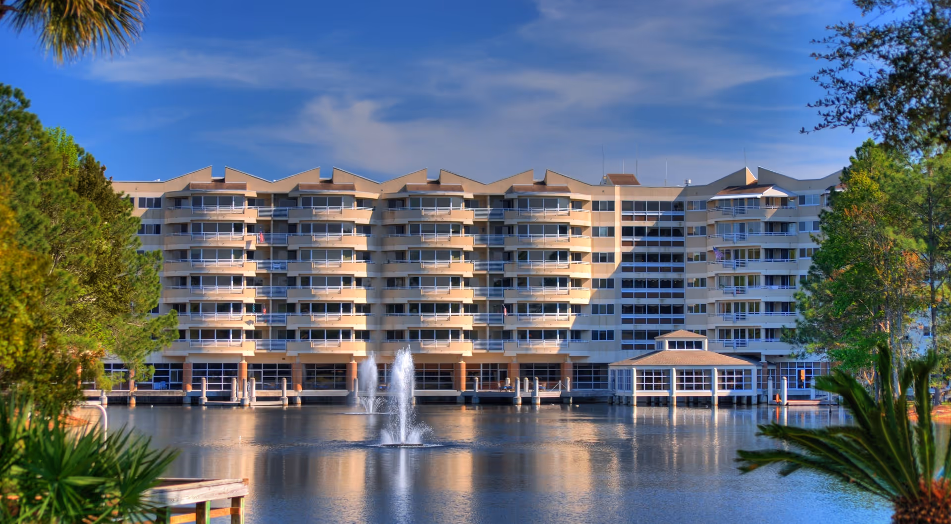 Large multi-story waterfront residence with rows of balconies facing a lake and a central fountain.