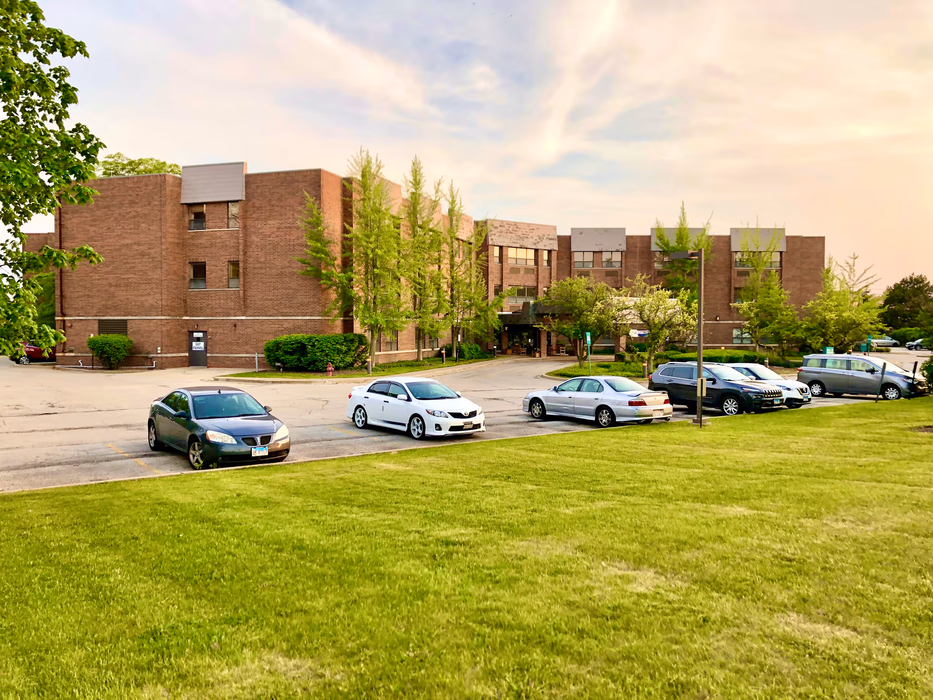 Exterior view of Elevate Care Abington, brick senior living building with a parking lot and lawn.