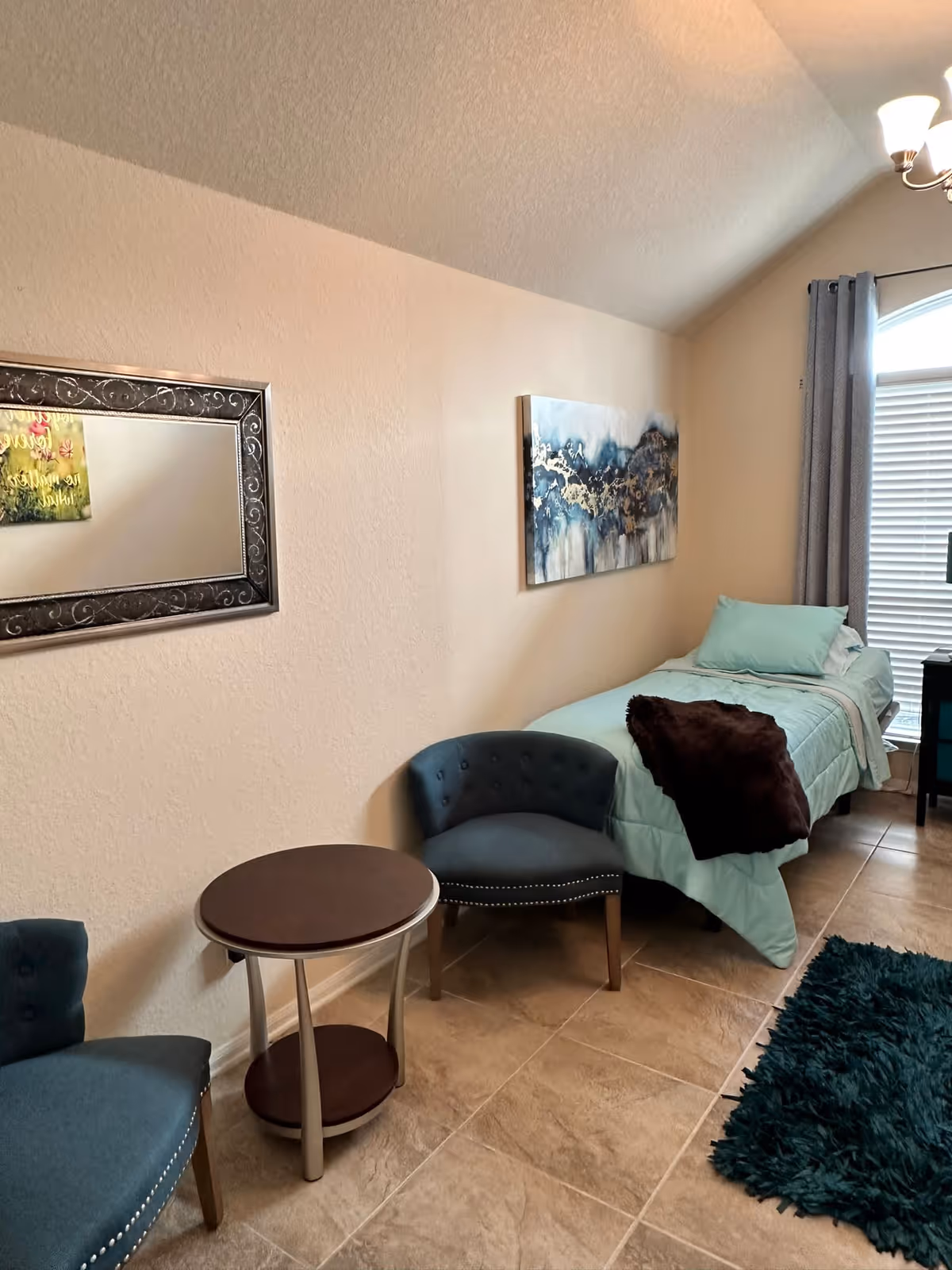 A cozy senior living bedroom with a single bed, seating, and wall art.