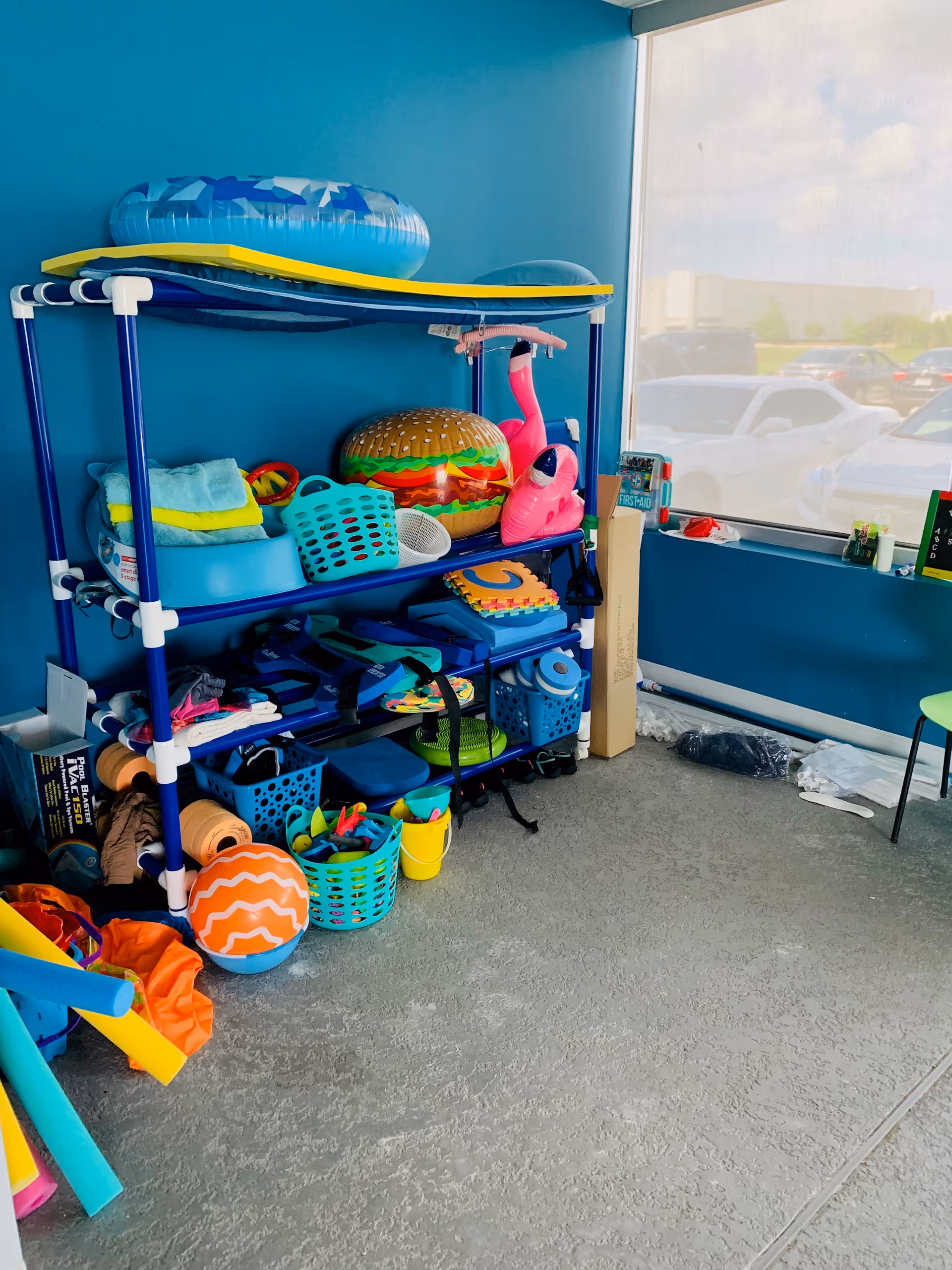 Interior storage area with blue walls and shelves of pool toys and play gear.