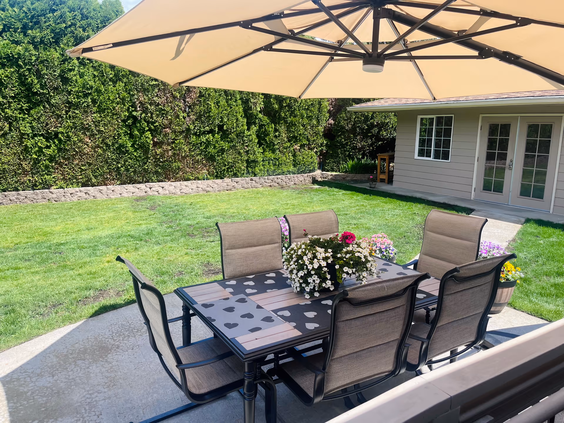 Outdoor patio with a table, six chairs, and a large umbrella in a sunny backyard.