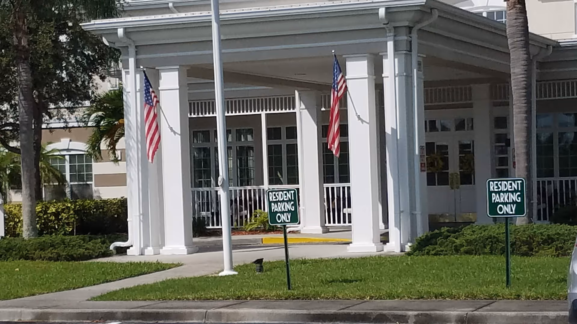 Exterior view of a senior living facility entrance with white columns and American flags