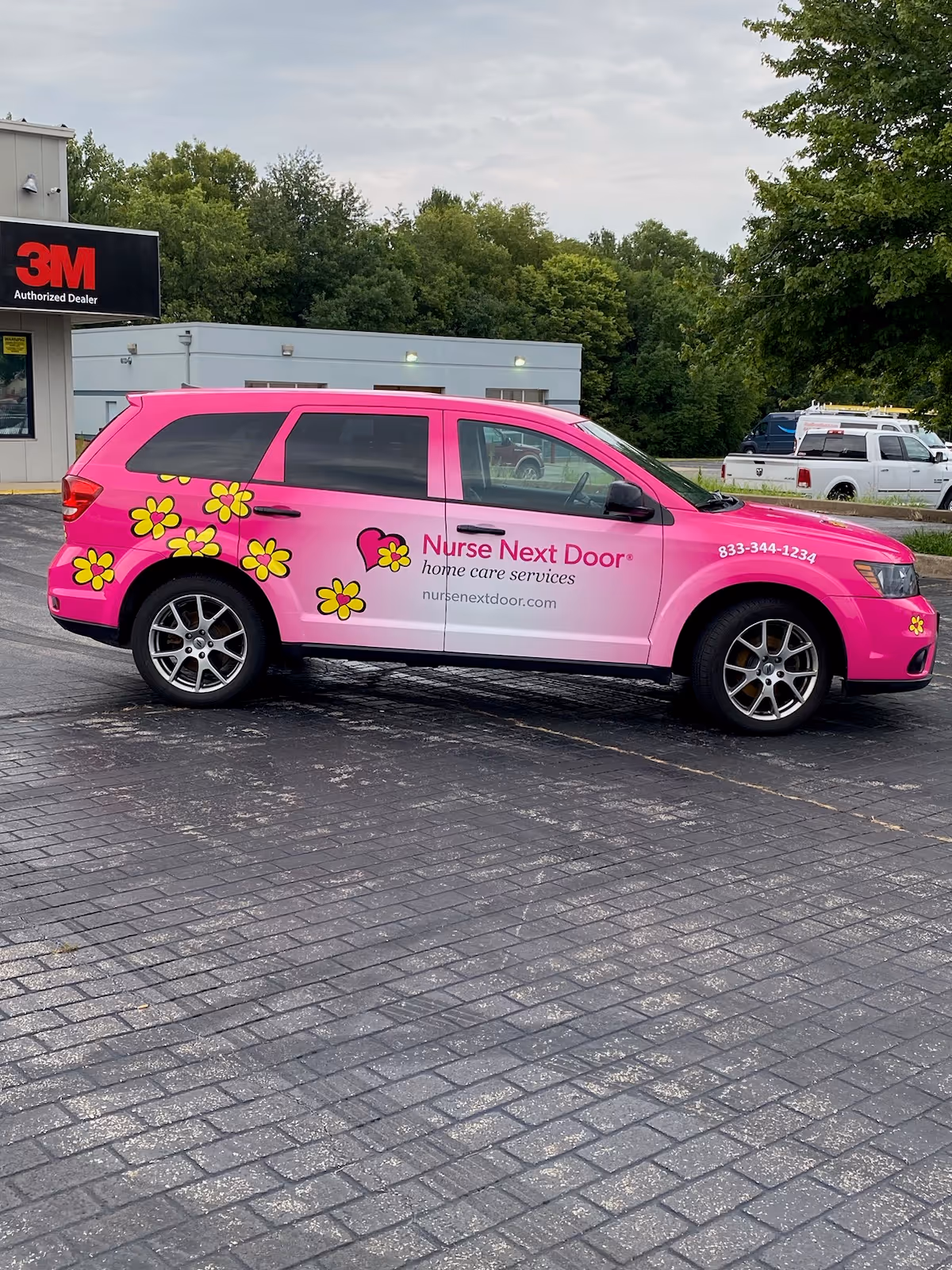 Bright pink Nurse Next Door van with yellow flower decals in a parking lot.