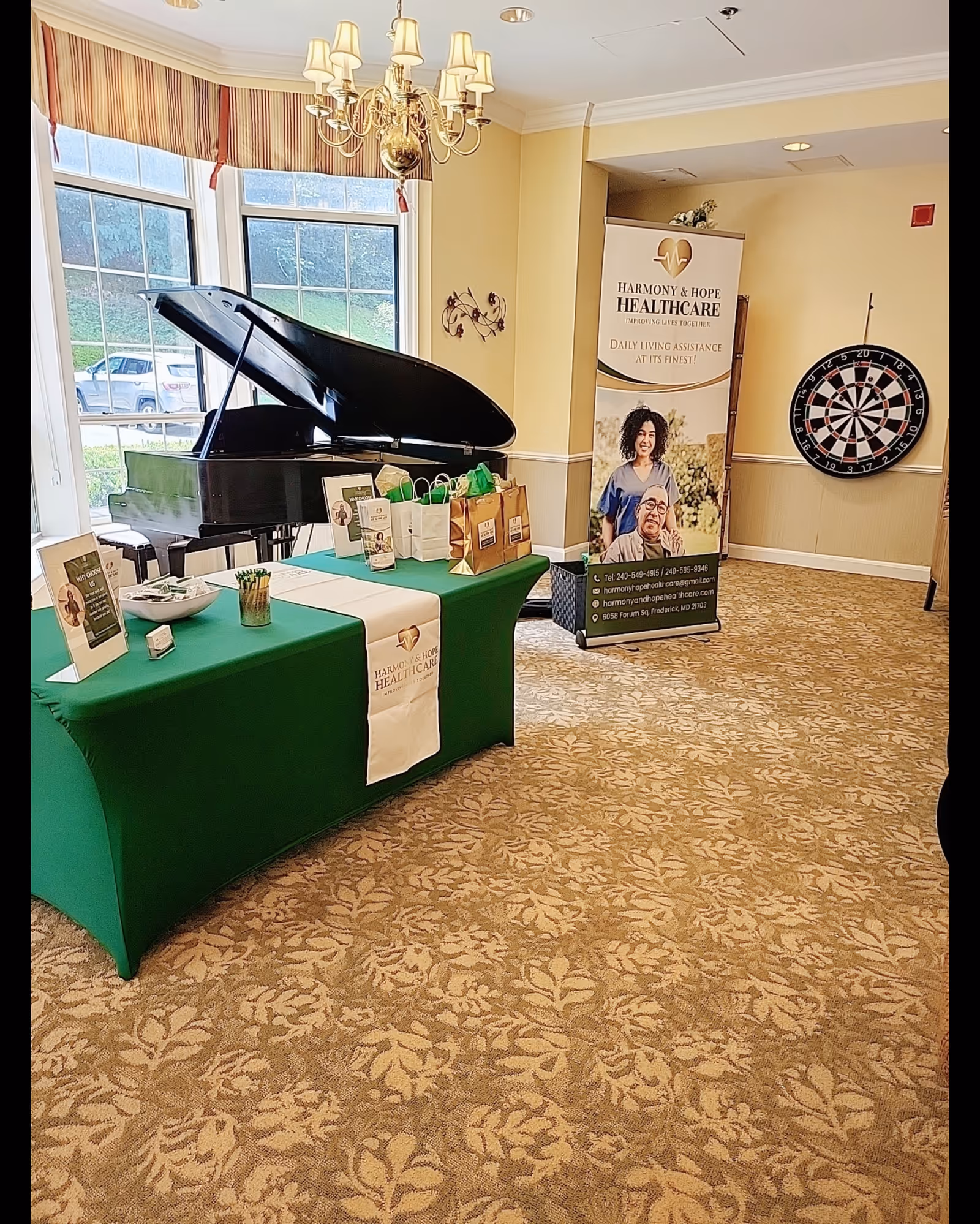 Grand piano beside a green-covered table with bags and a banner in a bright lobby.