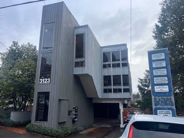 Gray angular multi-story building with tall windows and a covered driveway in front.