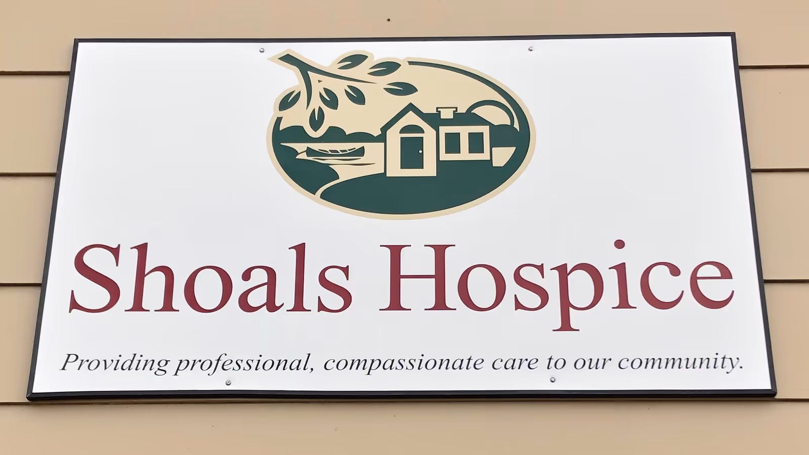 A large Shoals Hospice sign with logo mounted on a beige exterior wall