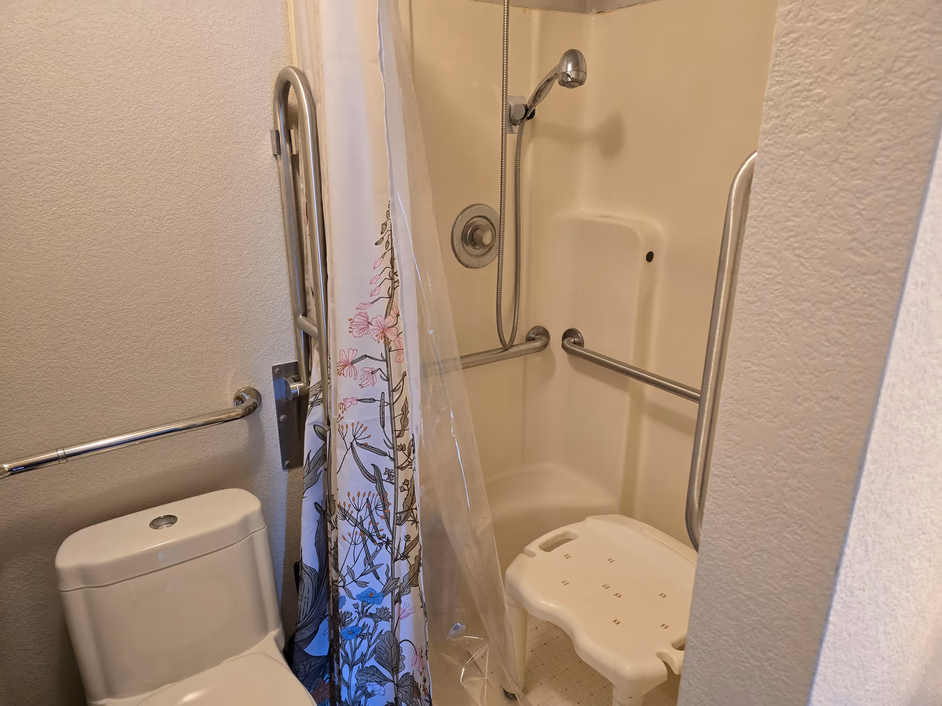 Accessible bathroom featuring a shower stall with grab bars, a curtain, and a shower chair.