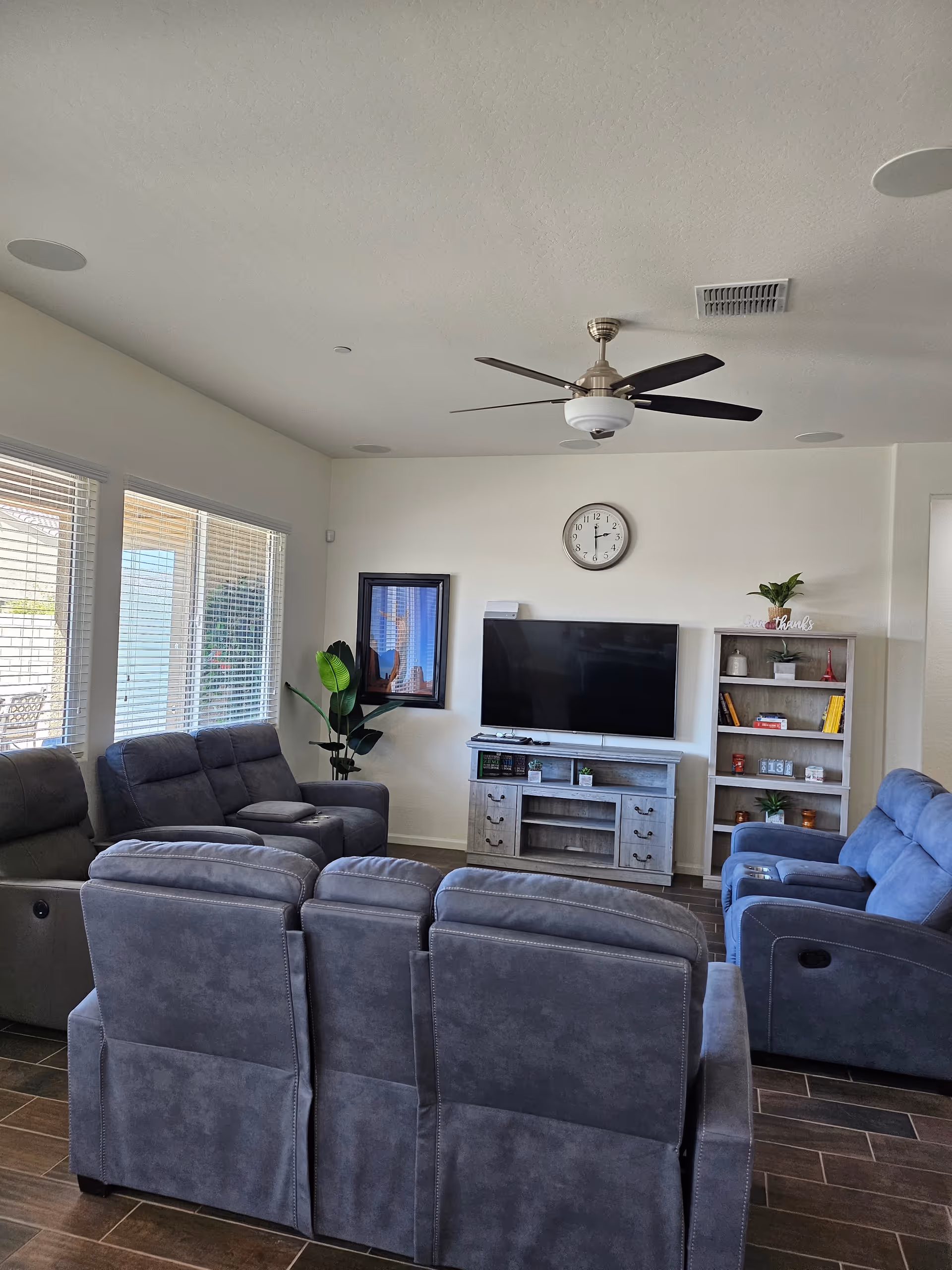 Spacious living room with blue recliners, TV stand, bookshelf, and ceiling fan.