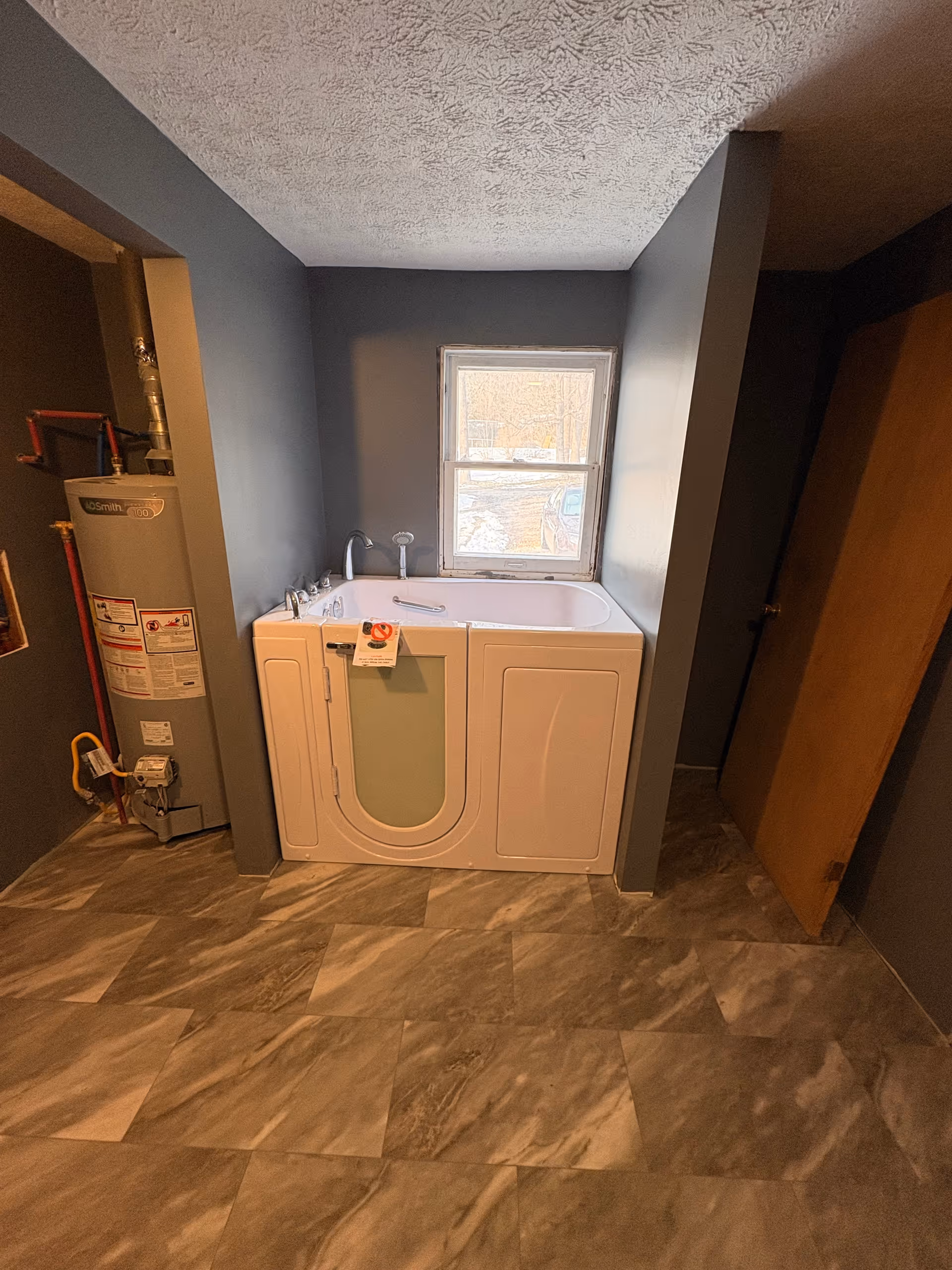 Gray bathroom features a white walk-in tub beneath a small window; heater on left.