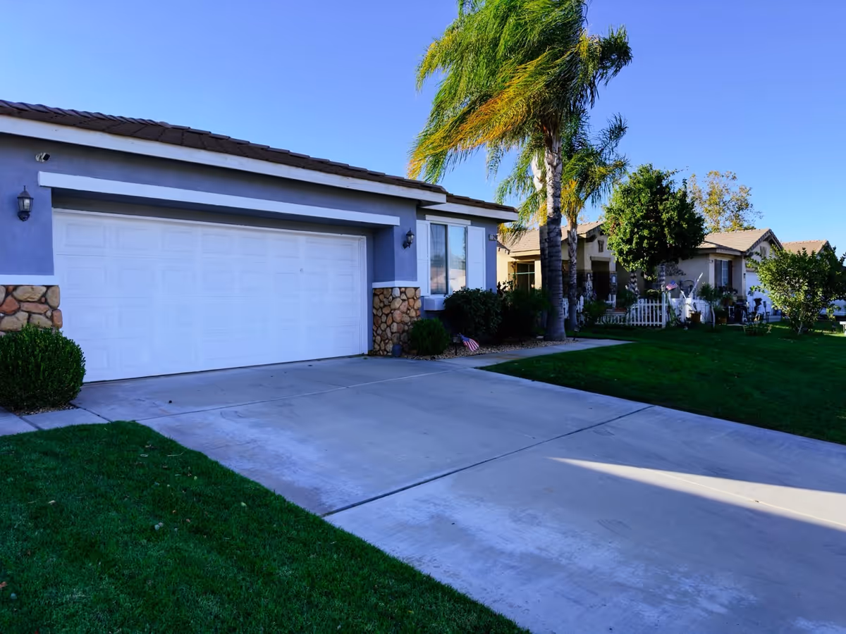 Front exterior of a single-story senior living home with palm trees and a driveway.