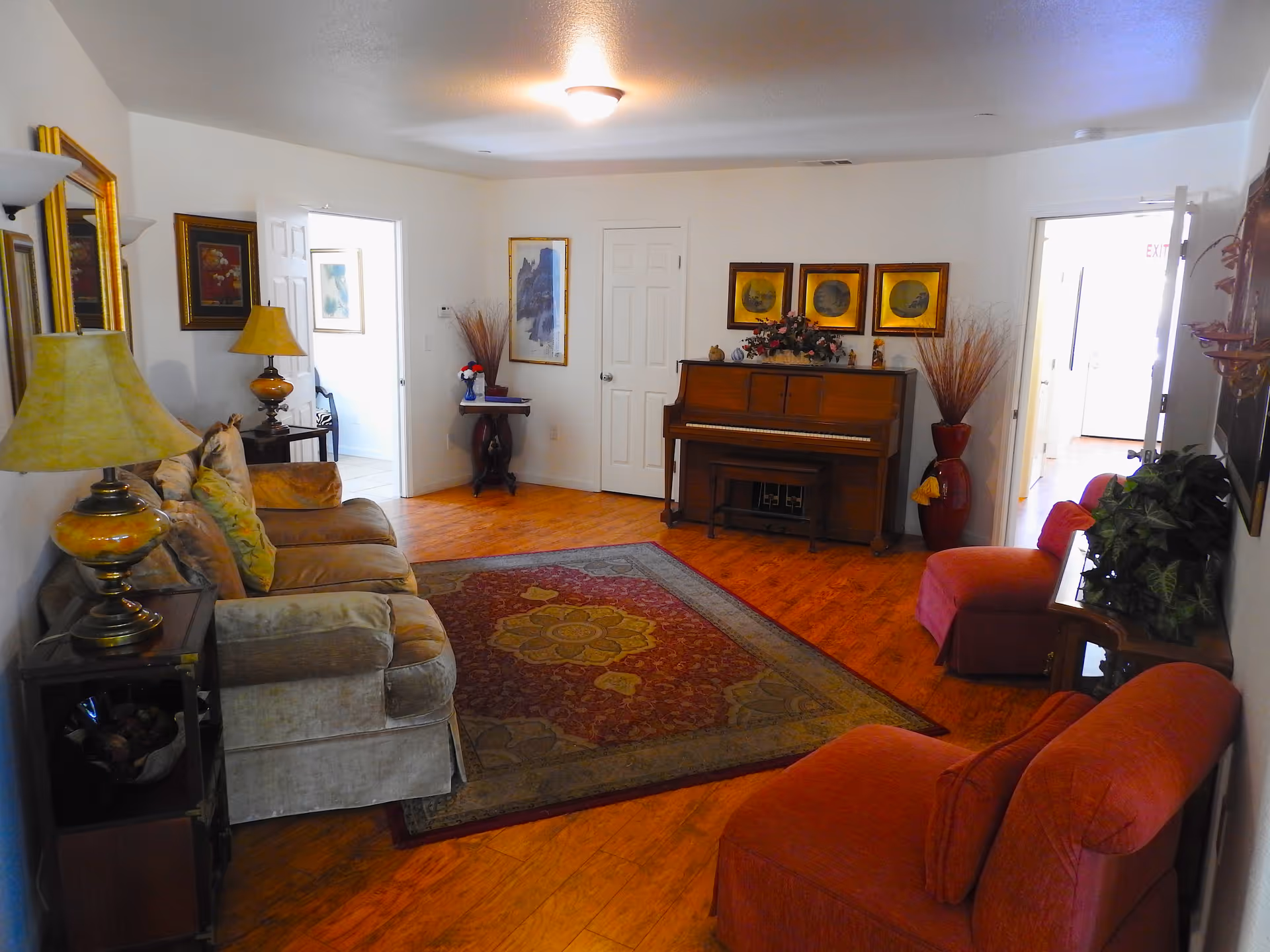 Cozy living room with beige sofa, red chairs, piano, rug, and decorative artwork.