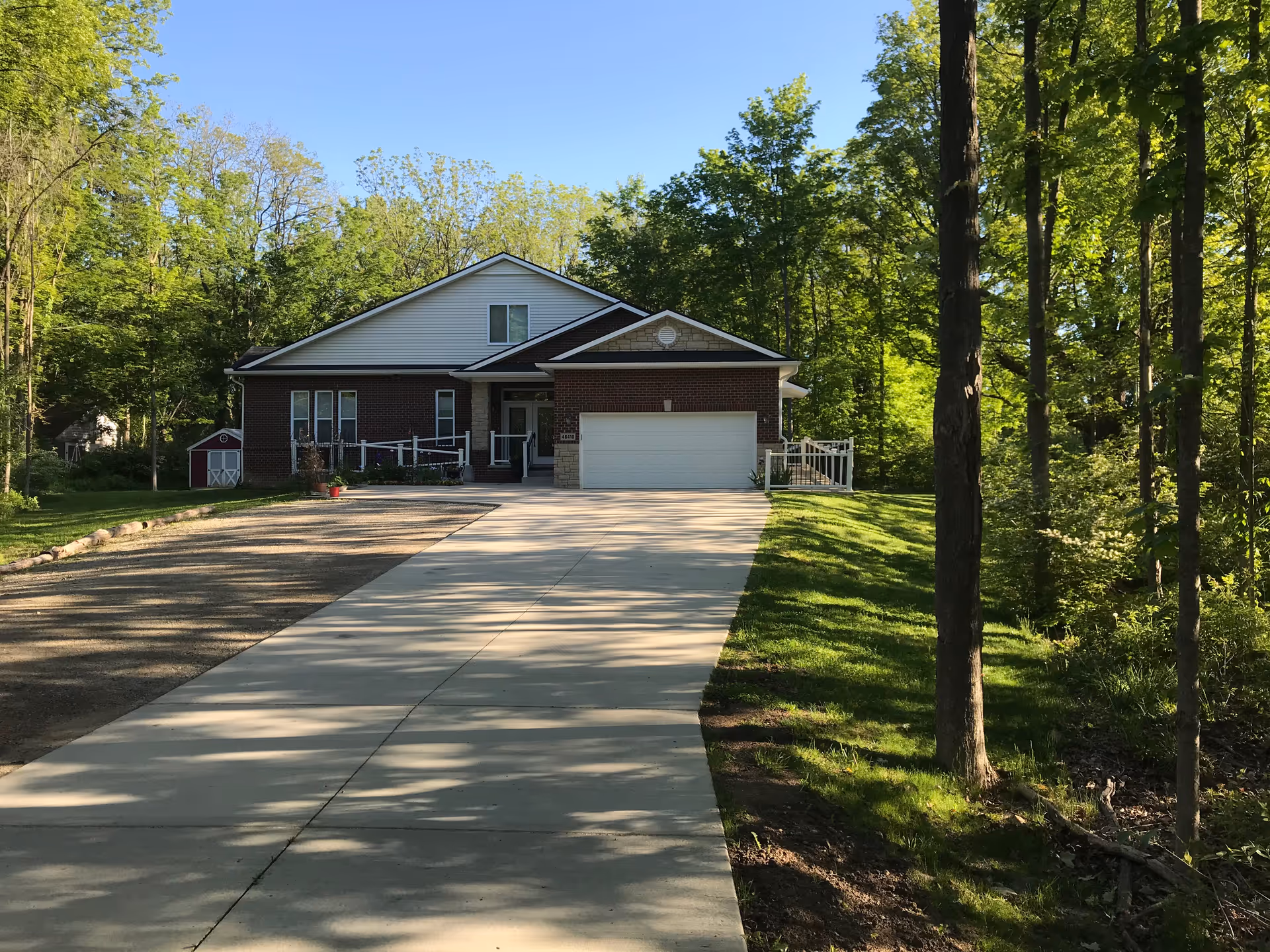 Sunny exterior of Serenity Manor of Canton with brick facade, driveway, and trees.