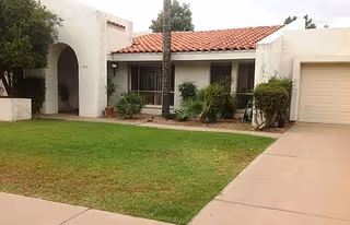 Front exterior of a single-story building with a lawn, driveway, and potted plants.