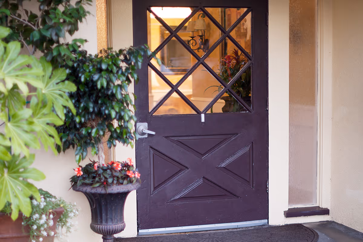 Dark wooden front door with diamond-pane glass, potted plants, and a welcome mat at the entrance.