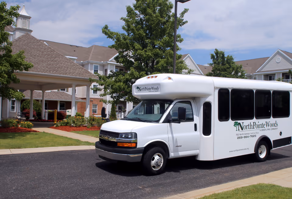 White bus parked in front of NorthPointe Woods building with landscaped entrance.