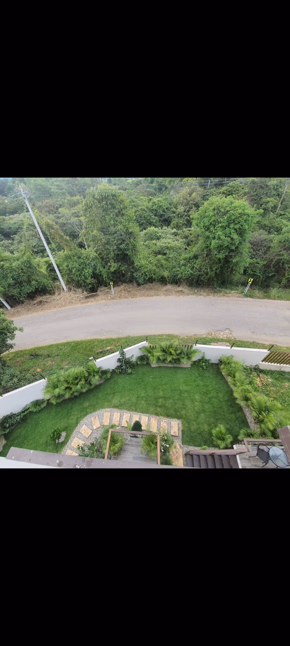 Aerial view of a green outdoor yard with a lawn, hedges, and a stone path.