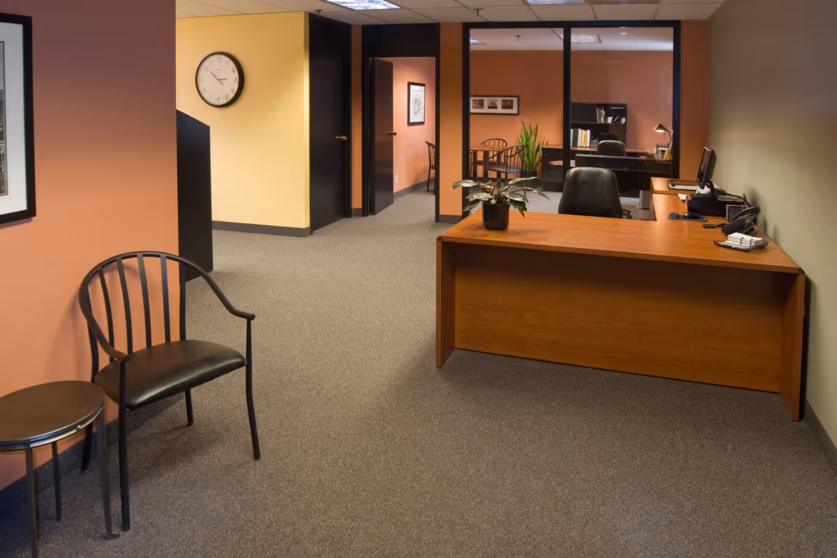 Reception desk with chair, plant, and hallway leading to offices in a warm interior.