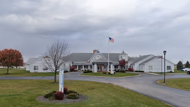 Exterior view of Gardens At Celina senior living facility with circular driveway and flag.