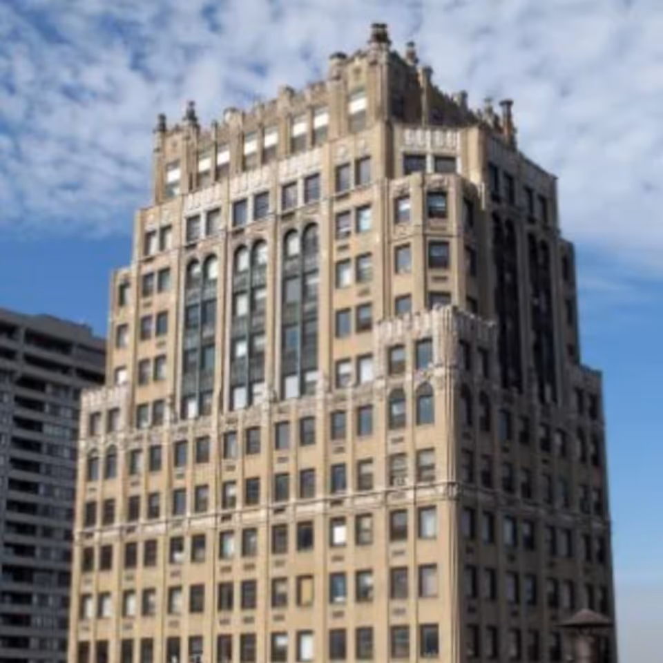 Tall, ornate beige apartment building with decorative setbacks against a blue sky.