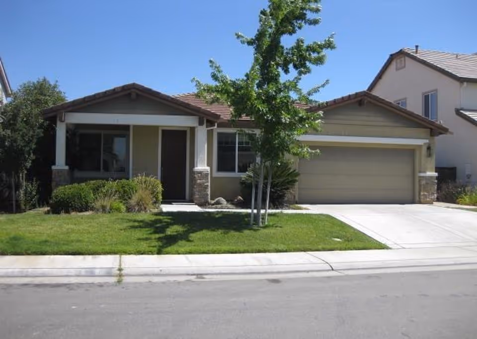 Single-story suburban home with a front lawn, driveway, two-car garage, and a small tree.