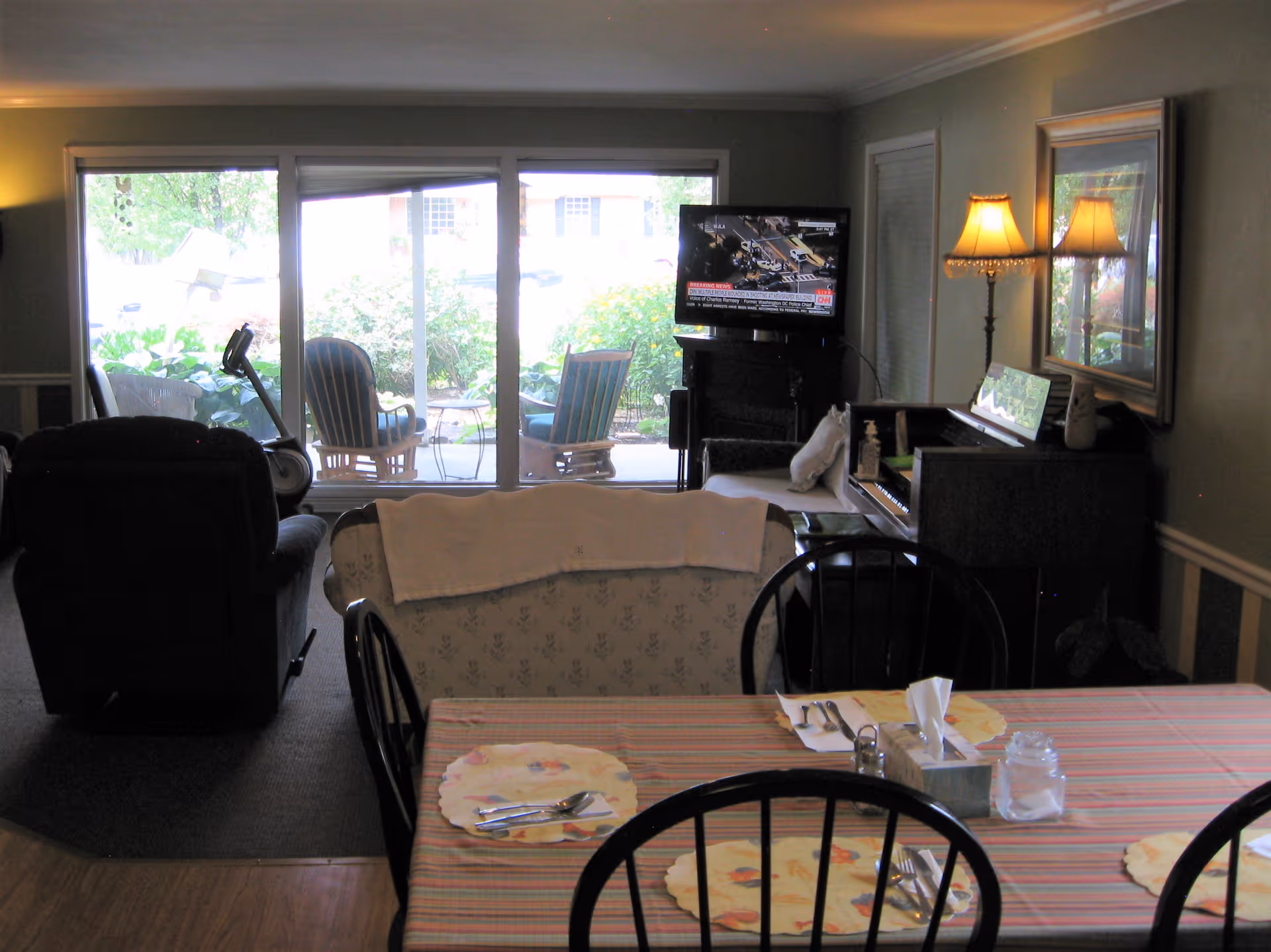 Cozy living area with sofa, TV, piano, dining table, and sliding glass doors to outdoors.
