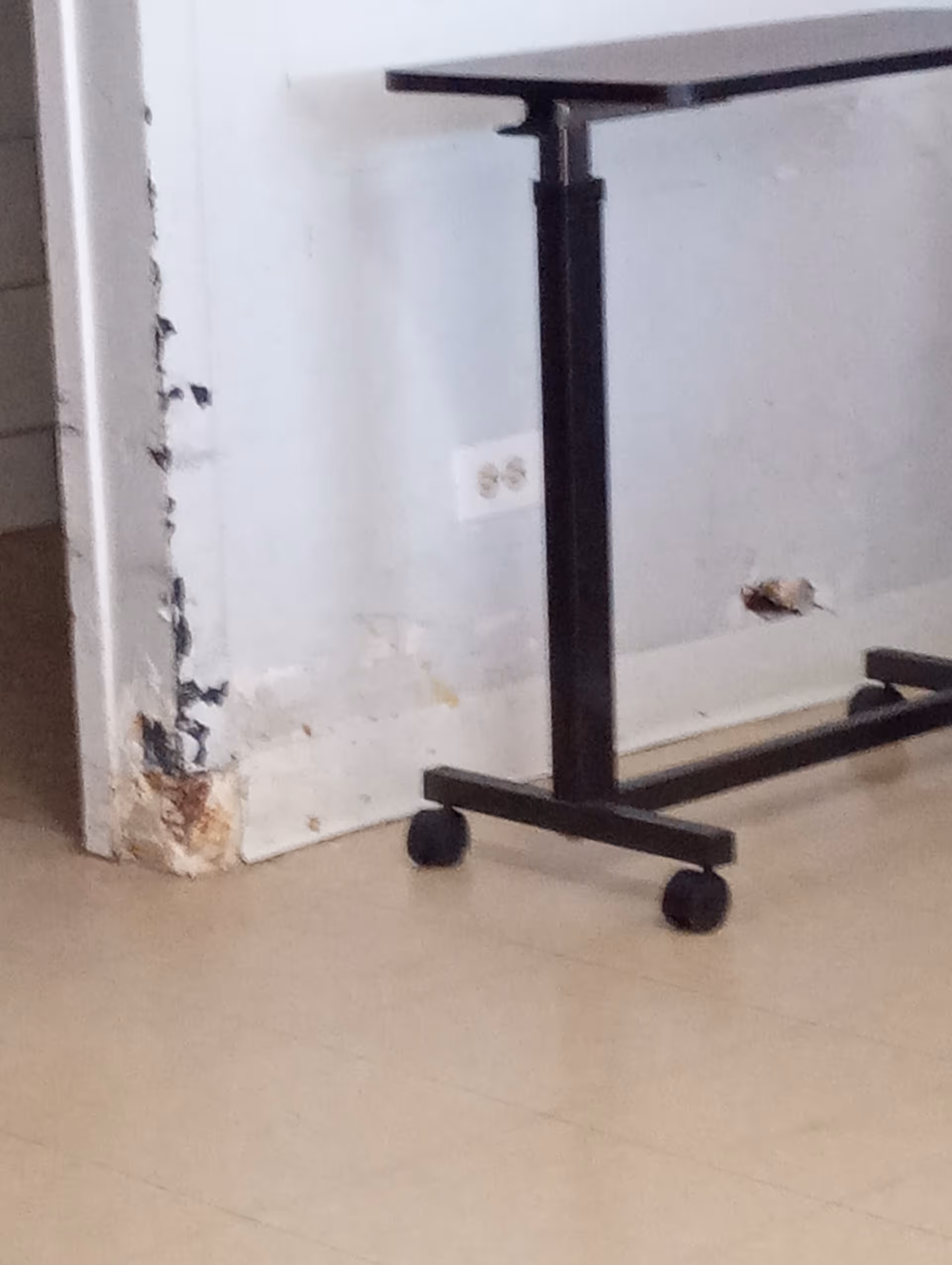 Interior room corner featuring a wheeled table base and damaged wall.