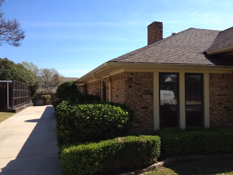 A brick senior living facility exterior with a walkway, hedges, and a windowed entrance.