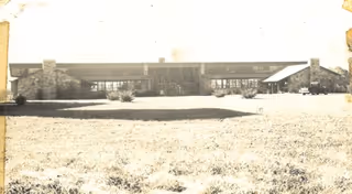 Long, low-slung mid-century building with a large front lawn.