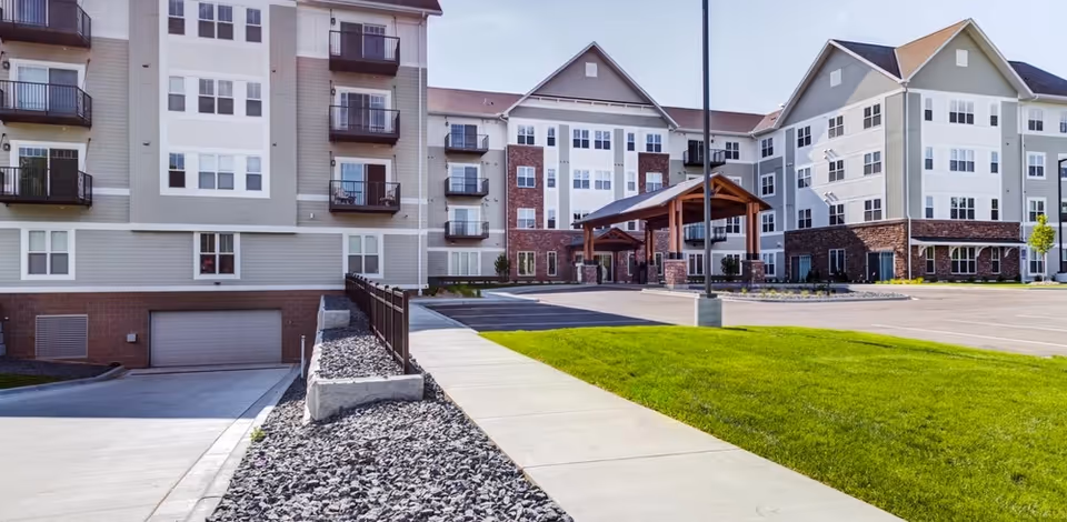 Exterior view of a multi-story senior living building with a pavilion and green lawn
