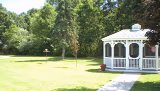 A white gazebo sits on a well-kept lawn at Ethan Place, surrounded by trees.