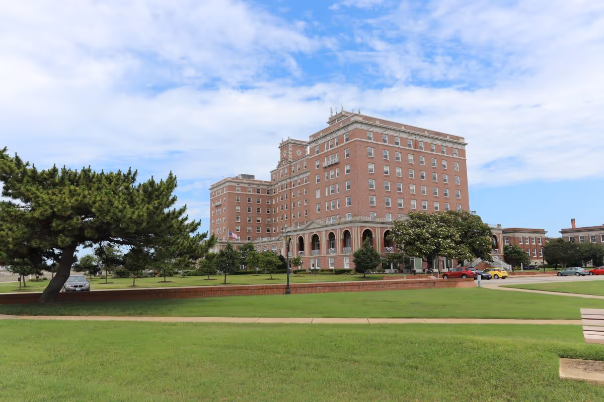 Exterior view of a tall brick senior living building with green lawn and trees.