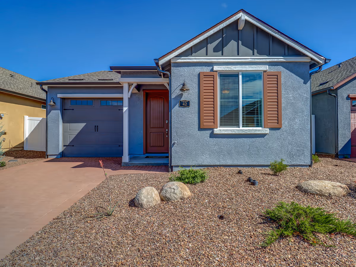 Front view of a blue-gray, single-story house with brown shutters and an attached garage.