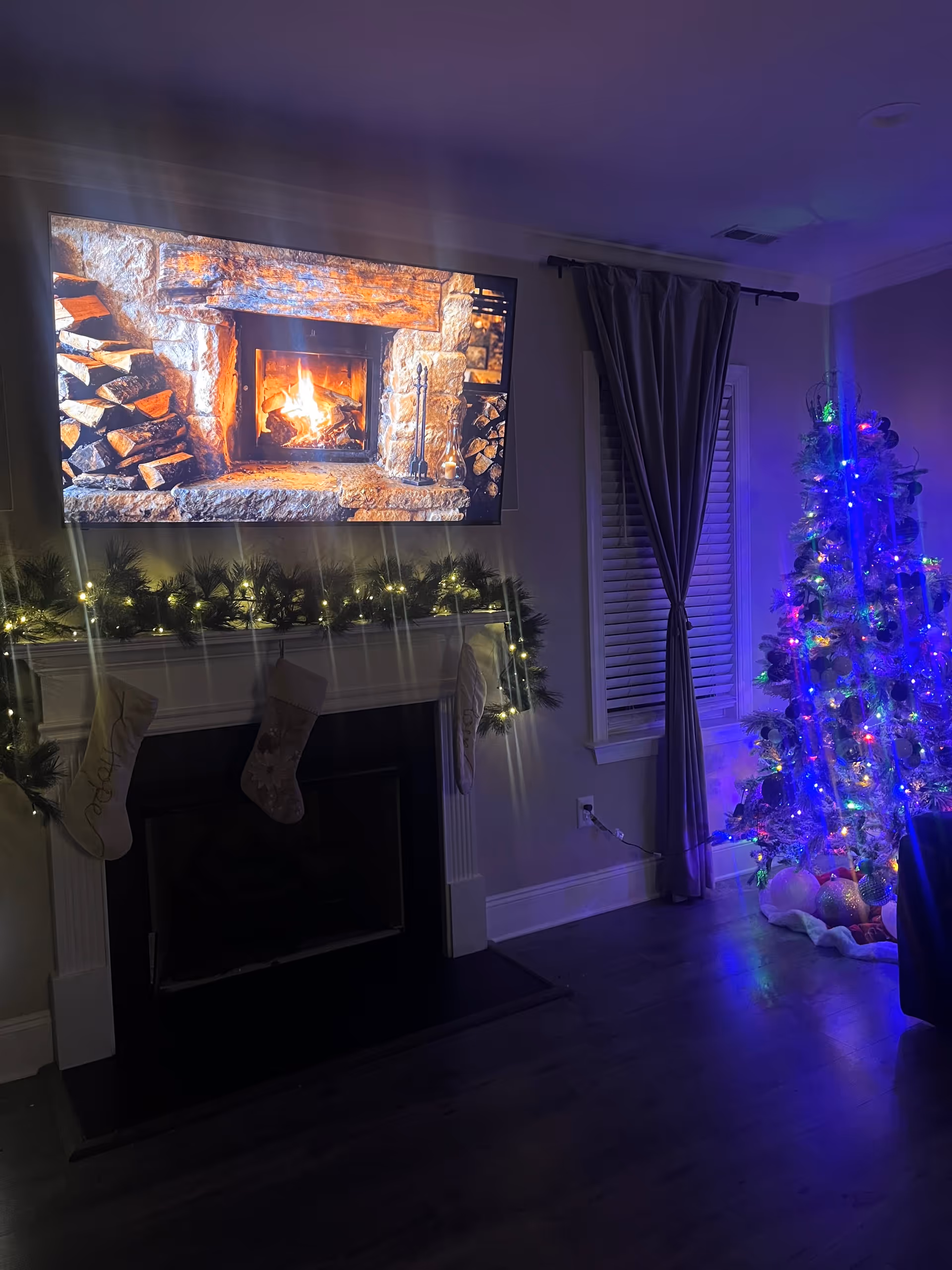 Cozy living room with a lit fireplace, garland, stockings, and a decorated Christmas tree.