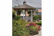 A gazebo sits beside a colorful garden path in front of a brick senior living building
