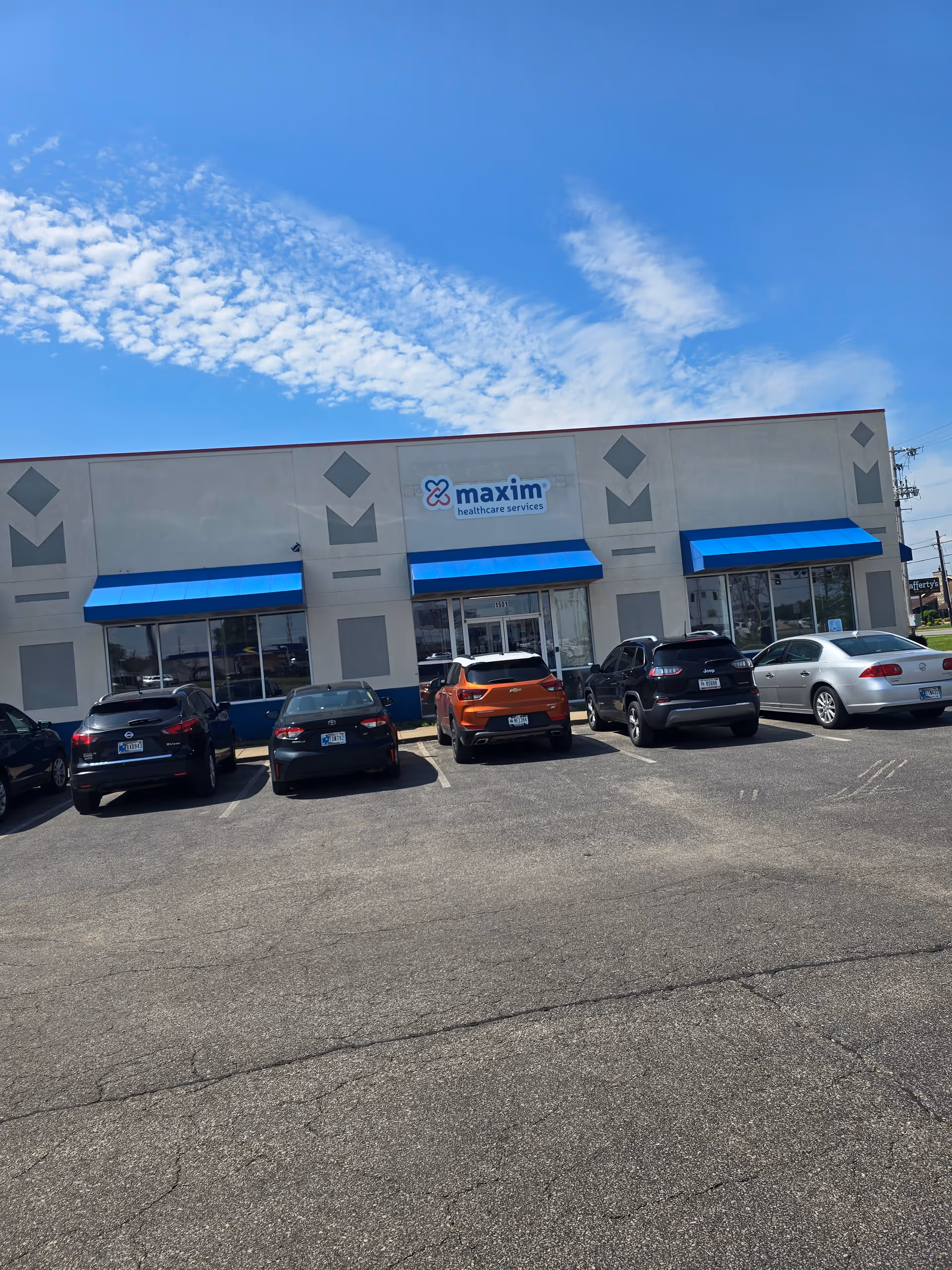 Facade of Maxim Healthcare Evansville regional office with blue awnings and parked cars.
