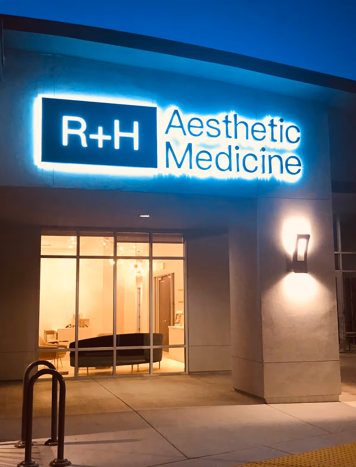 Nighttime exterior of a building with a glowing R+H Aesthetic Medicine sign.