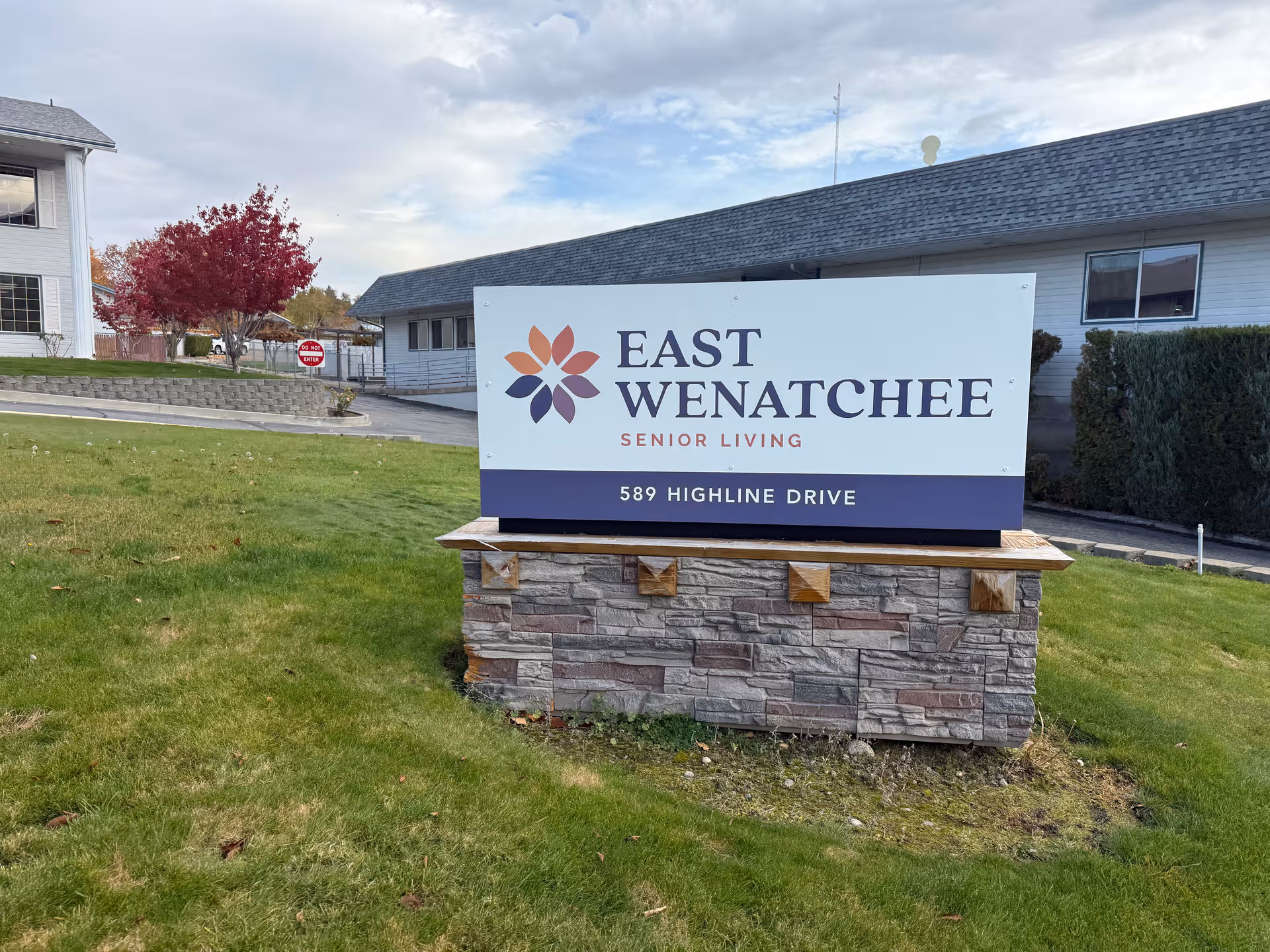 Exterior view of East Wenatchee Senior Living sign with building and grassy lawn.