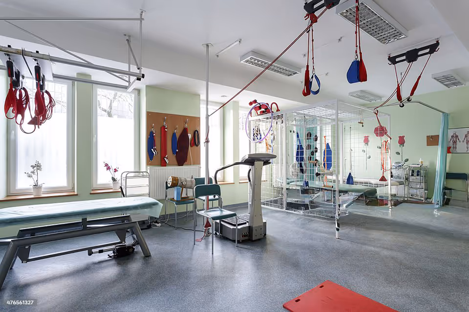 Rehabilitation therapy room with exercise equipment, hanging straps, mats, and therapy beds.
