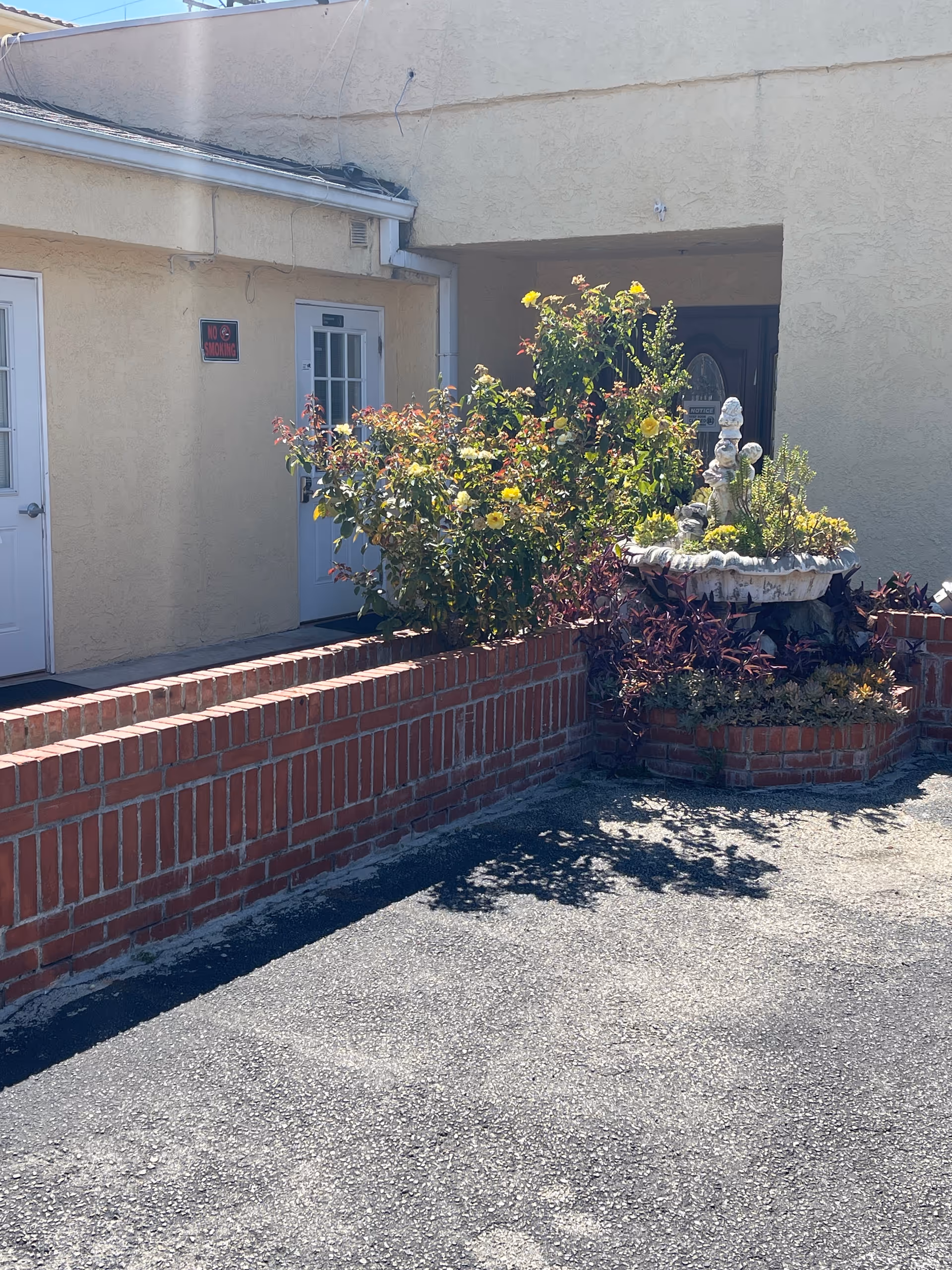 Exterior view of a beige senior living facility with a brick planter and flowers