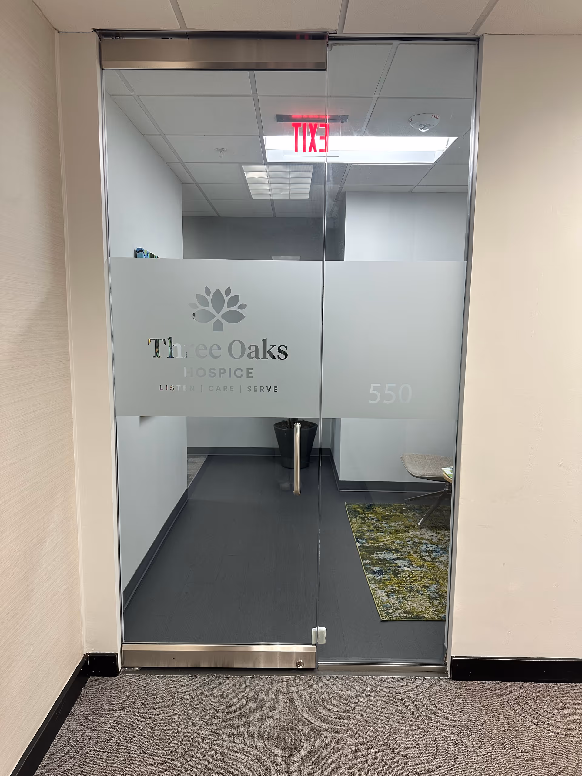 Glass door entrance to Three Oaks Hospice interior with frosted logo and hallway.