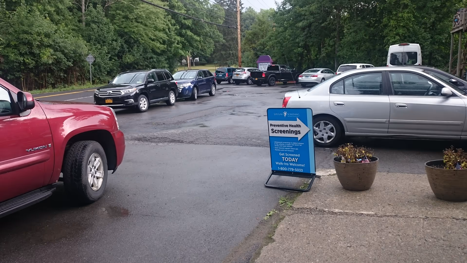 Parking lot outside Hearthstone Care facility with cars and a blue health screening sign