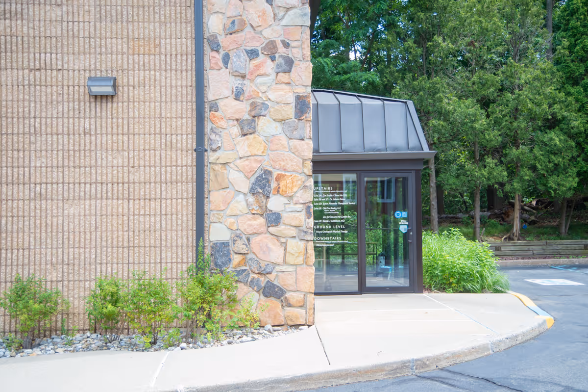 Exterior entrance with glass doors, stone feature, brick wall, and surrounding greenery.