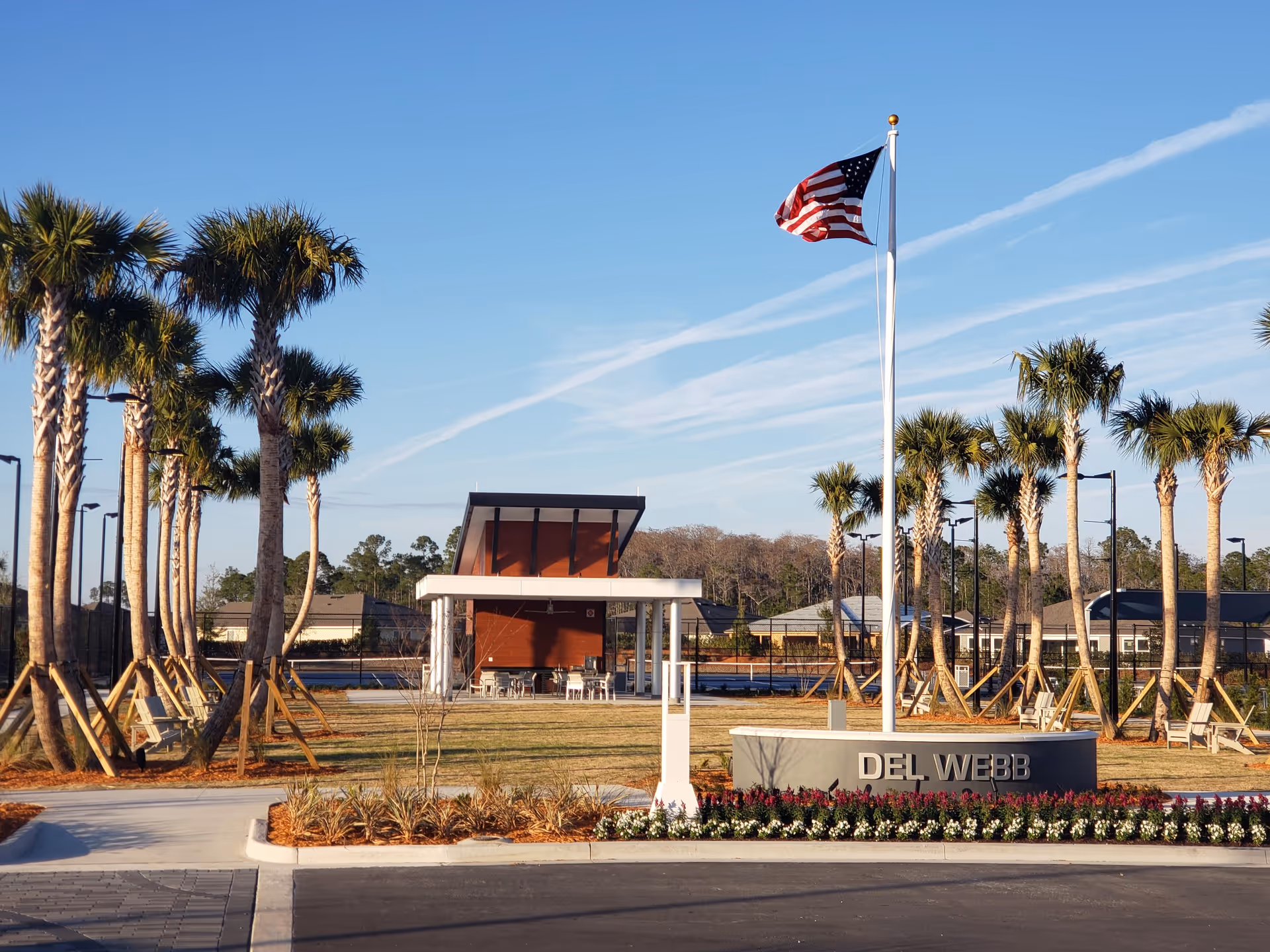 Outdoor view of Del Webb Etown entrance with flag, palm trees, and plaza.