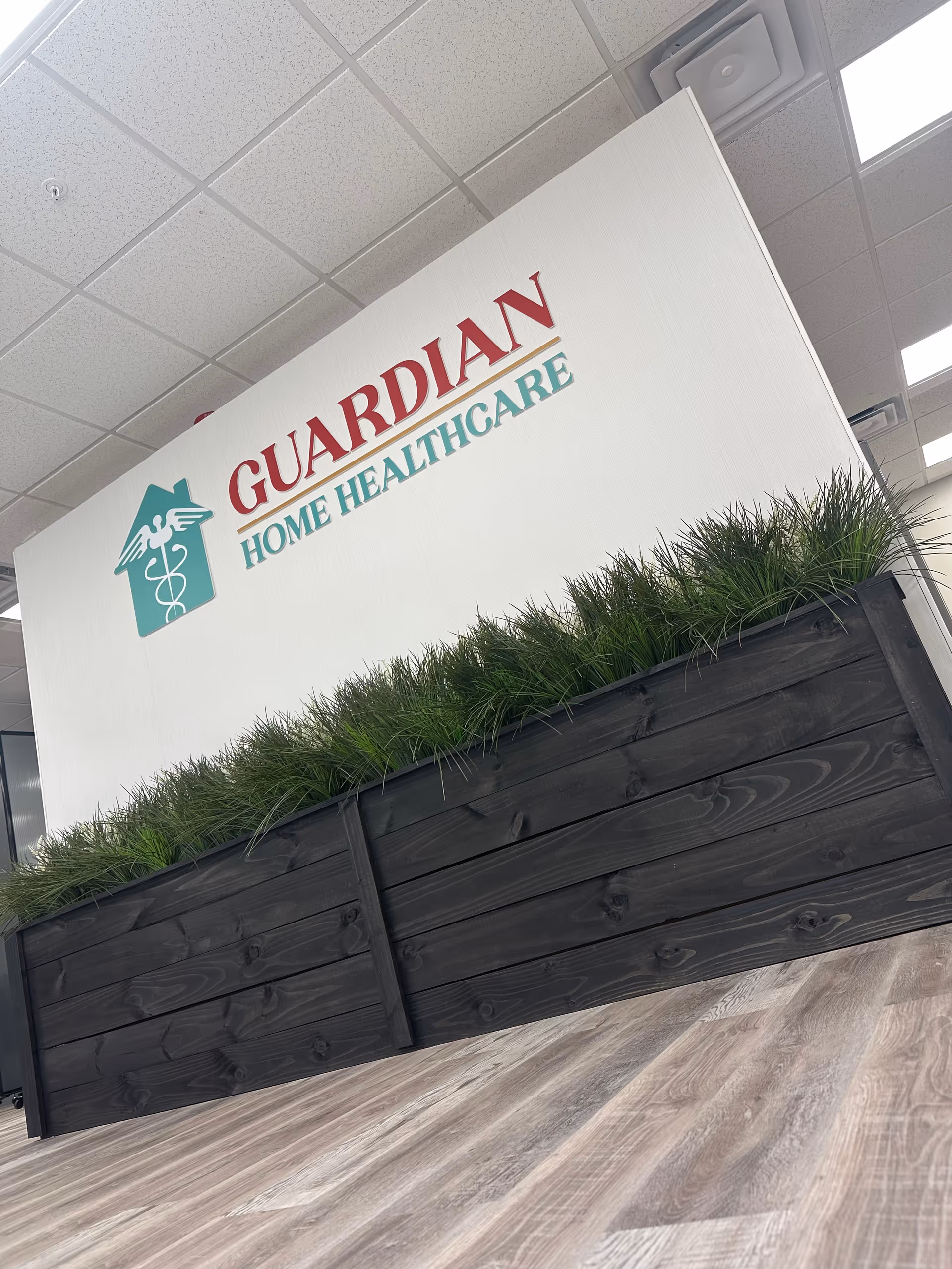 Interior space featuring a Guardian Home Healthcare sign and a black planter with green grass.