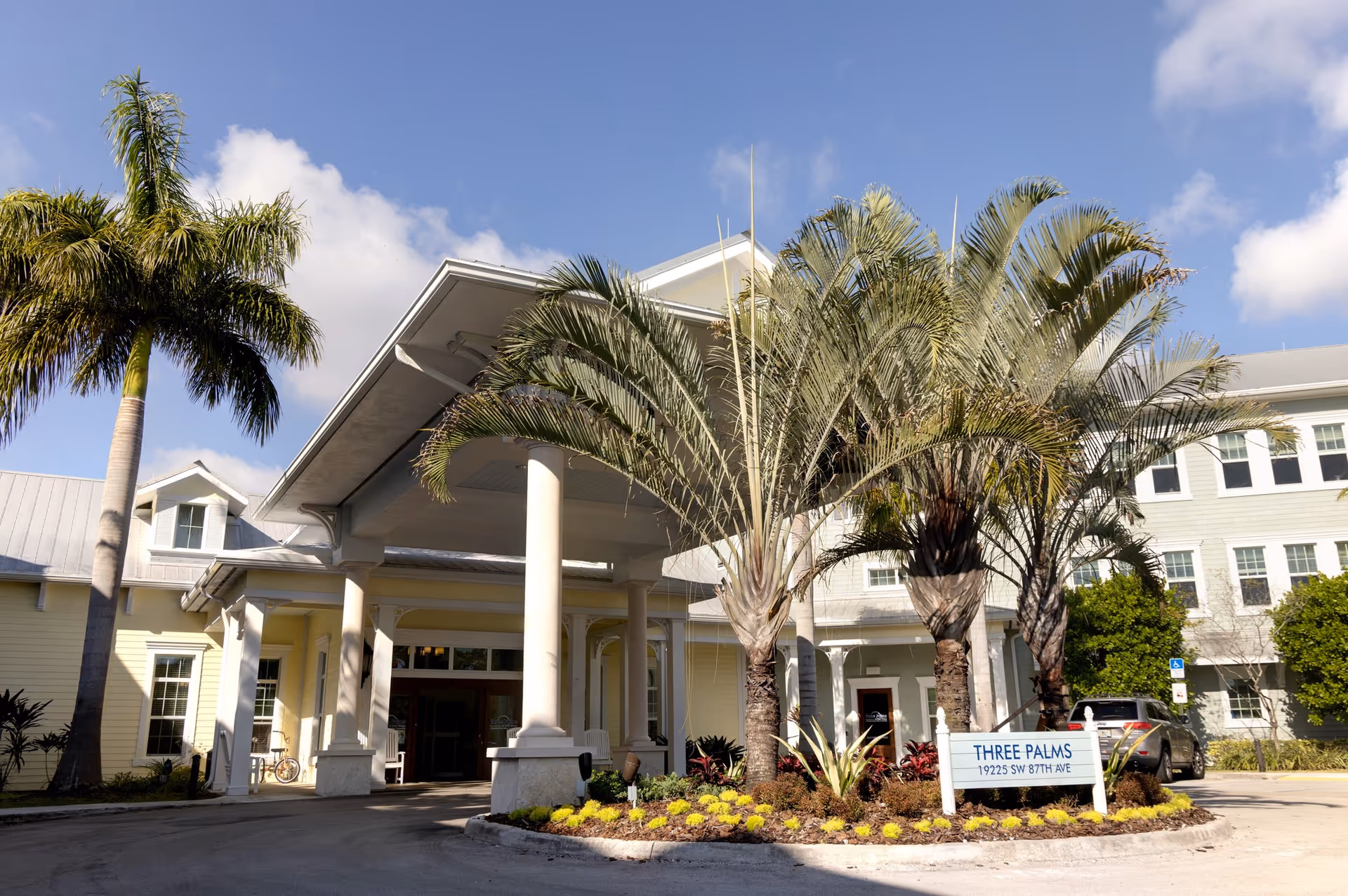 Exterior of a senior living facility with palm trees, a covered entrance, and a circular driveway.