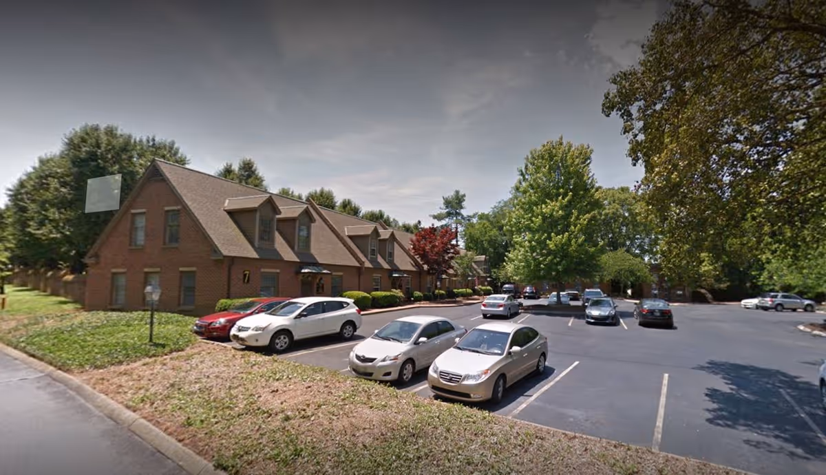 Exterior view of a brick senior care facility with a parking lot and trees.