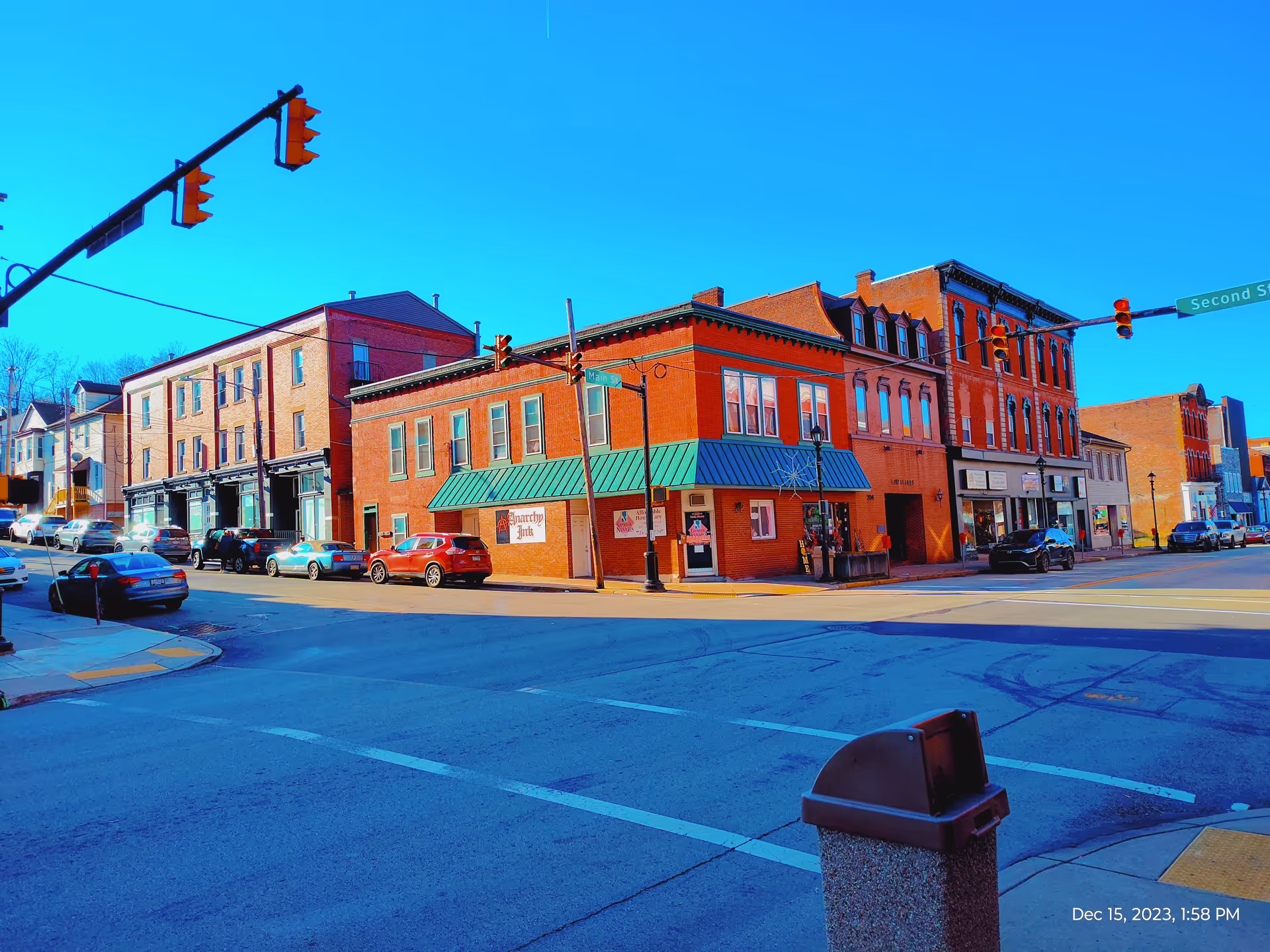 Colorful downtown street with brick storefronts, parked cars, and a clear blue sky.