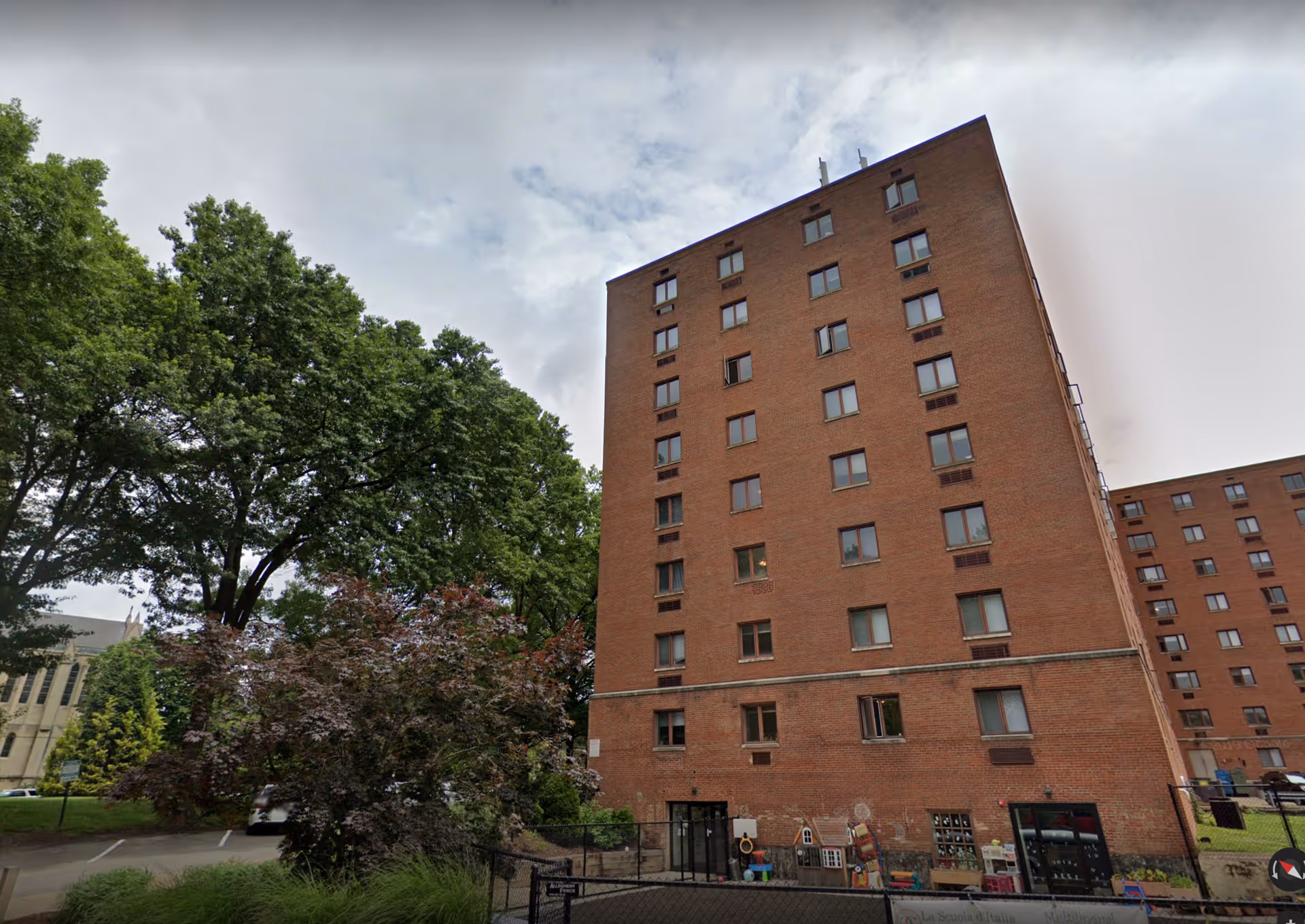 Tall brick senior living building with trees and a ground-level entrance