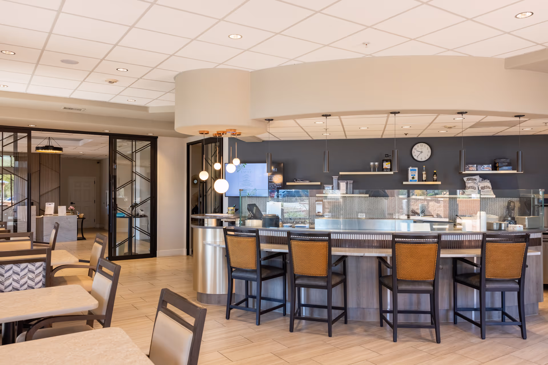 Interior dining area with curved counter, glass barrier, and bar stools.