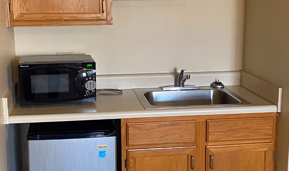 Small kitchenette with microwave, sink, and wooden cabinets in a senior living facility.